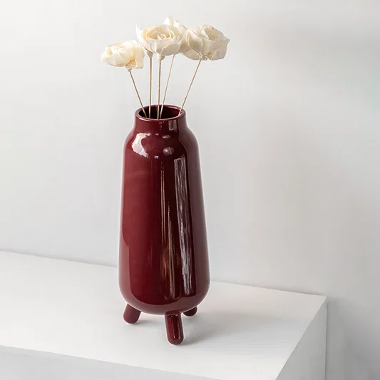 Elegant burgundy vase placed on a minimalist white shelf highlighting its tall structure and deep red hue for contemporary home décor.