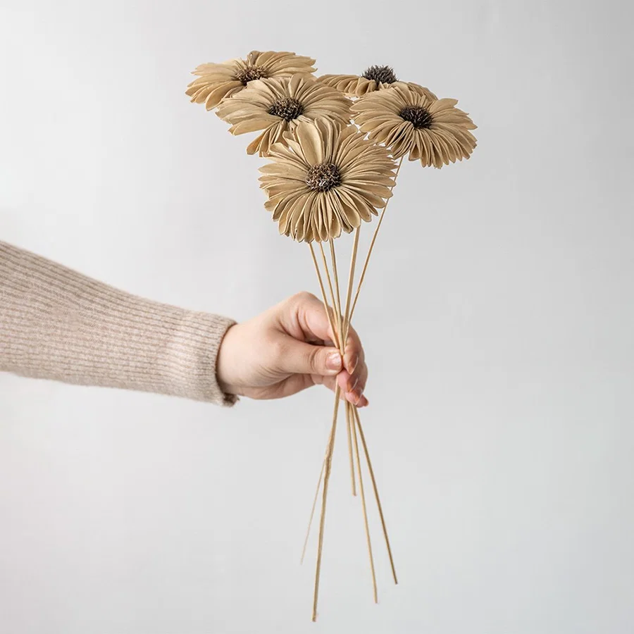 Hand holding five natural jute burlap handmade gerbera daisy flower stems for rustic farmhouse vase decor on white backdrop.