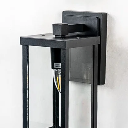 Closeup of outdoor wall light with black frame and transparent glass shade highlighting warm glowing bulb design.