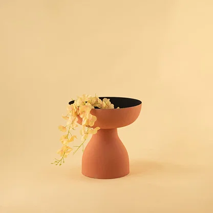 Terracotta orange pedestal bowl with black interior styled in a modern home setting adding warm artistic decor to shelves and tables.
