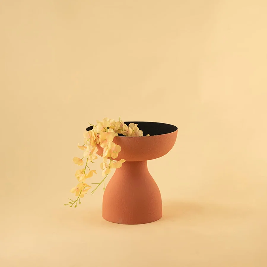 Terracotta orange pedestal bowl with black interior styled in a modern home setting adding warm artistic decor to shelves and tables.