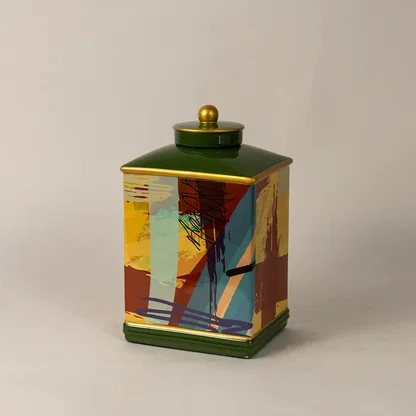 Decorative ceramic jar with colorful abstract design and green lid placed on white surface against neutral background showcasing stylish modern home decor accent.