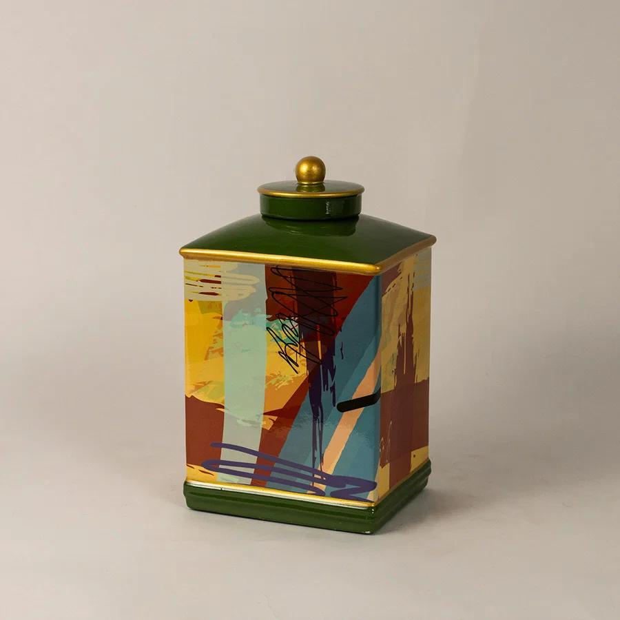 Decorative ceramic jar with colorful abstract design and green lid placed on white surface against neutral background showcasing stylish modern home decor accent.
