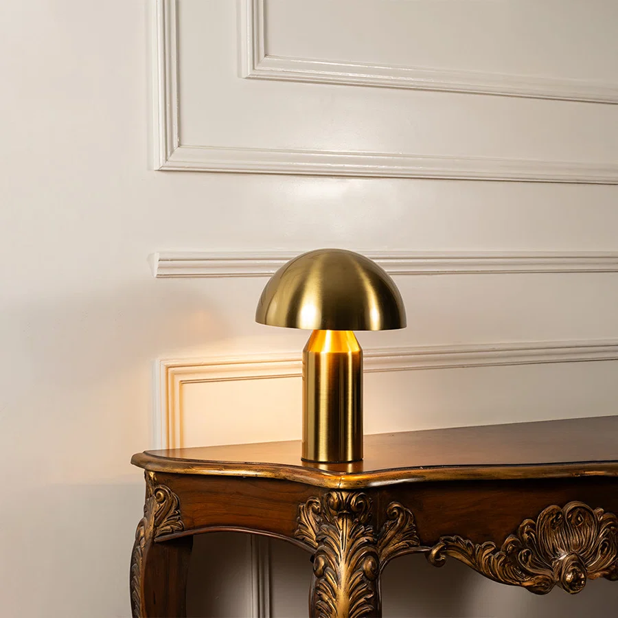 Gold metal mushroom table lamp displayed on a carved wooden console table creating elegant modern task lighting.