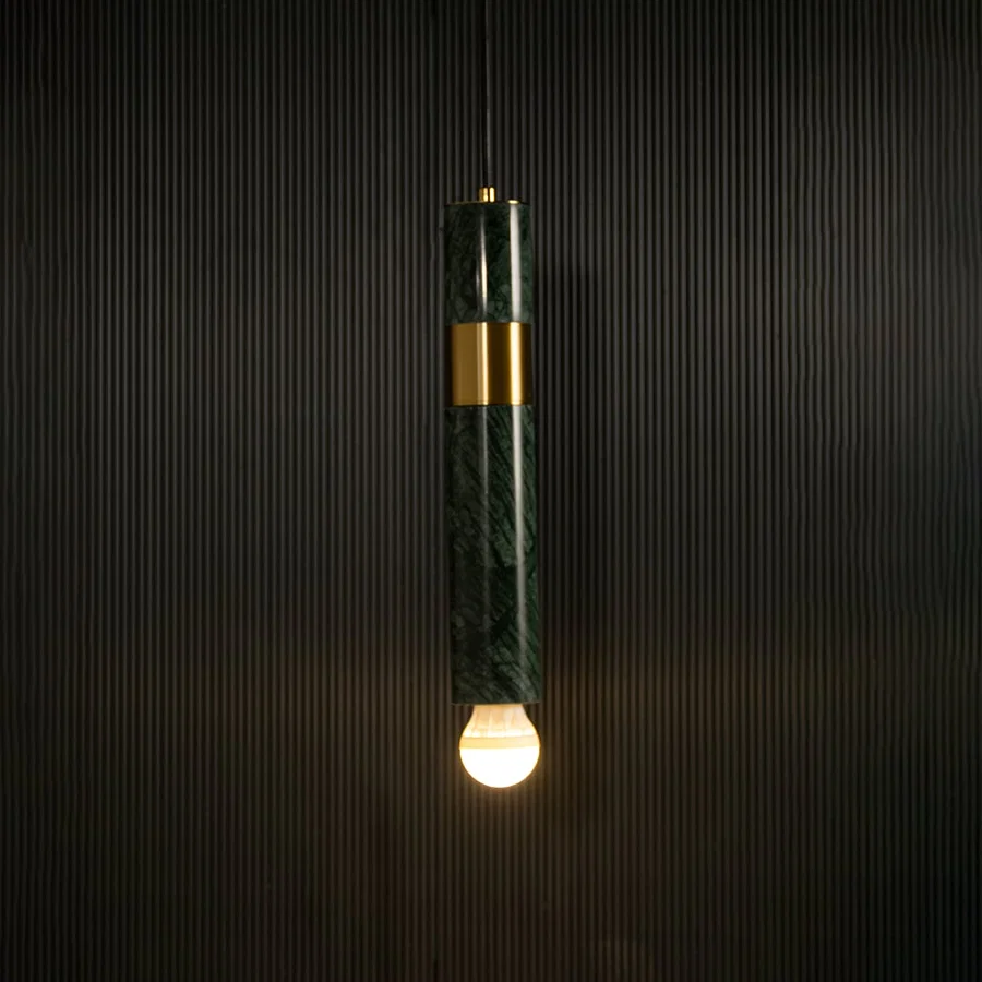 Green marble and metal cylinder pendant light with exposed bulb hanging against dark textured wall with light on for luxury modern décor.