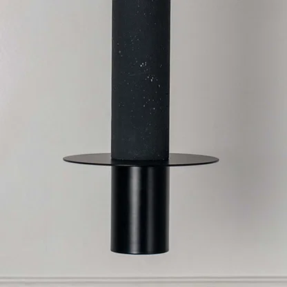 Black cylindrical pendant light with flat disc detail and matte finish hanging against neutral wall background highlighting sleek modern minimal lighting design.