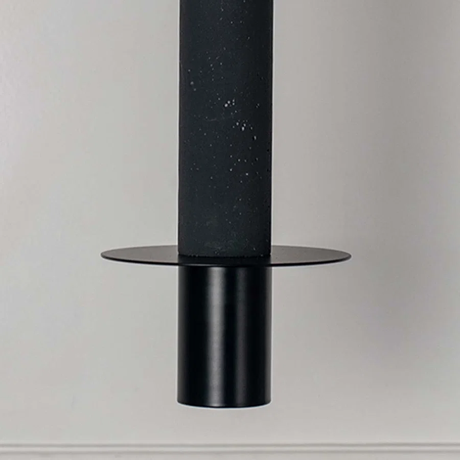 Black cylindrical pendant light with flat disc detail and matte finish hanging against neutral wall background highlighting sleek modern minimal lighting design.