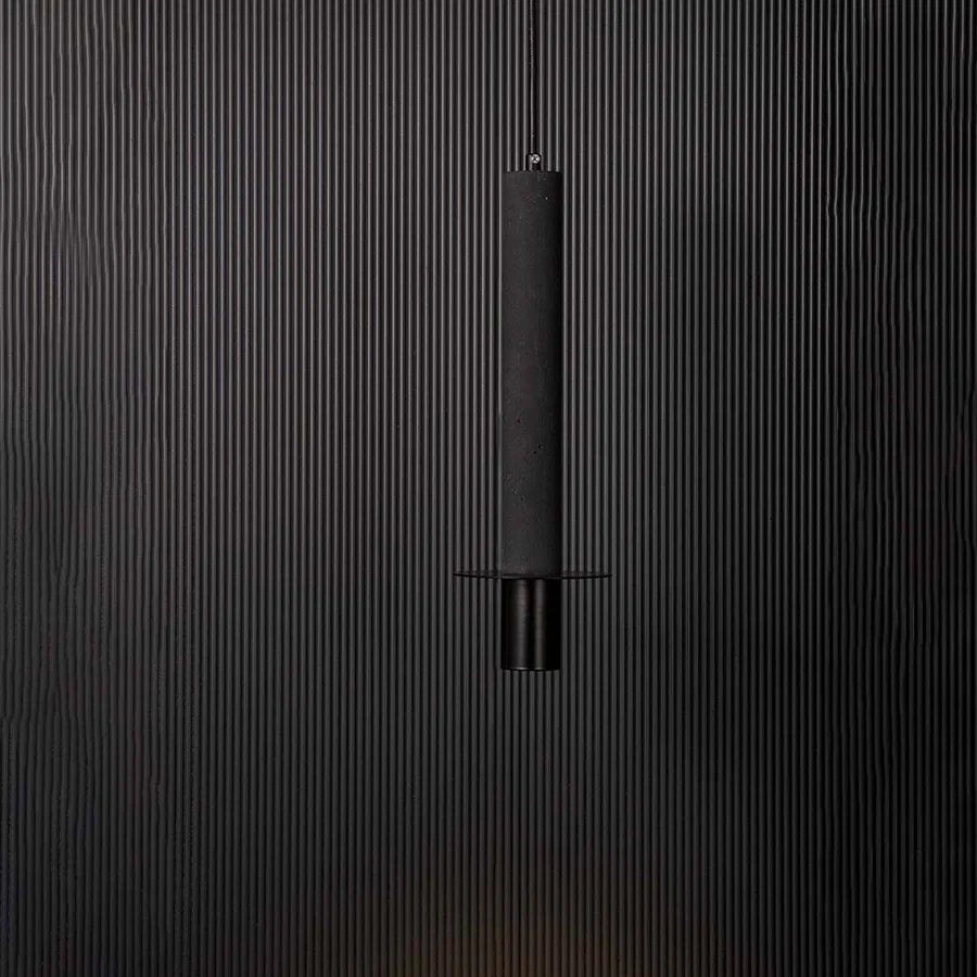 Black cylindrical pendant ceiling light glowing softly against black background creating a modern and elegant interior style.