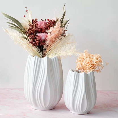 White ceramic vases with sculpted wavy texture displayed together on a soft pink surface filled with dried florals creating a calm modern Decor styling.