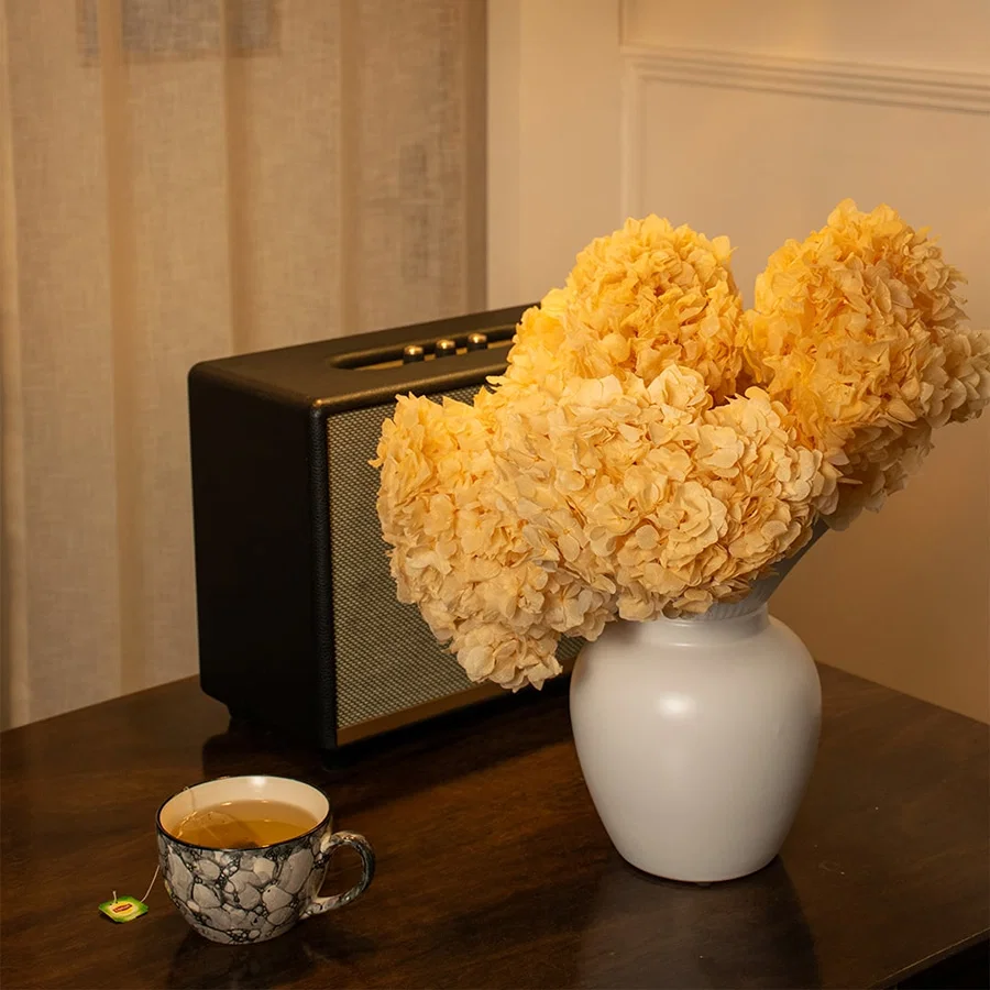 White ceramic vase with ruffled top filled with dried hydrangea flowers styled on wooden table adding cozy charm to living room decor.