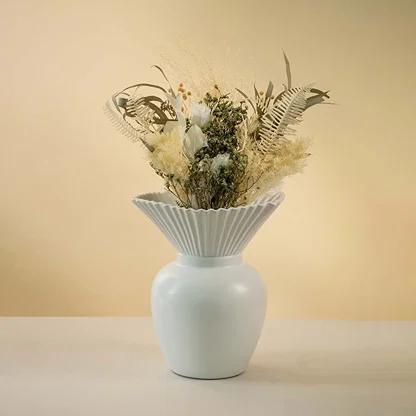 Modern white ceramic vase with pleated design styled with dried floral arrangement on wooden coffee table enhancing the elegant living room decor.