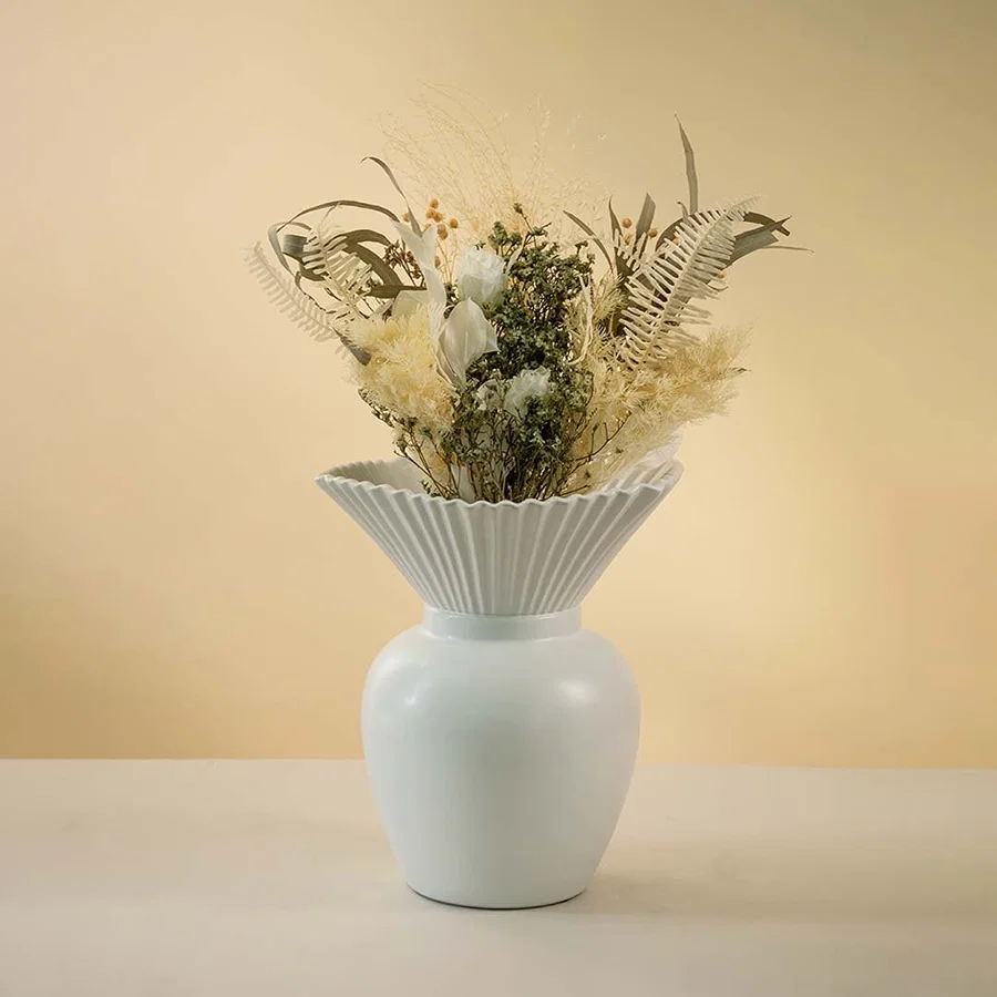 Modern white ceramic vase with pleated design styled with dried floral arrangement on wooden coffee table enhancing the elegant living room decor.