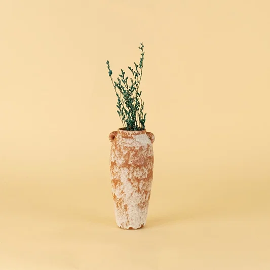 Rustic terracotta ceramic vase styled with greenery on wooden table against neutral wall for warm minimal interiors.