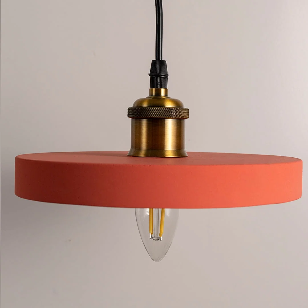 Detailed view of terracotta orange metal pendant light with refined gold accents and exposed bulb.