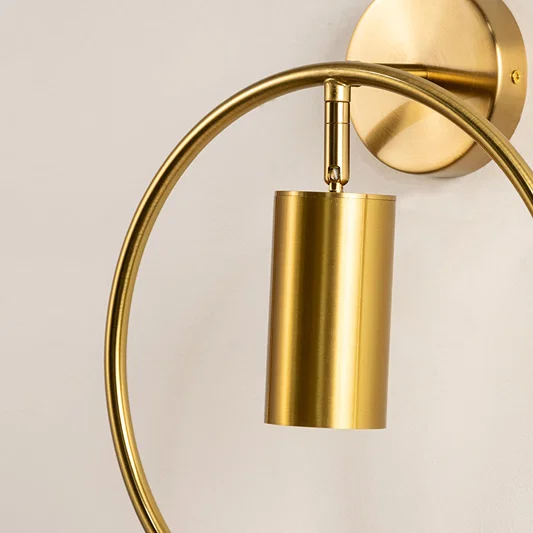 Closeup of gold metal wall light with curved arm and cylindrical shade showcasing sleek finish for modern interior decor styling.