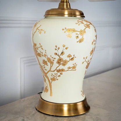 Table lamp closeup showing cream ceramic base with gold floral detailing and fabric shade for refined interior accents.
