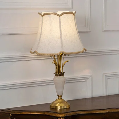 Gold and white marble base table lamp with cream fabric shade turned on against white background bedside table lamp.
