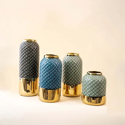 A collection of textured ceramic vases in grey blue and teal tones with glossy gold bases displayed together on a white background showcasing coordinated decor styling.
