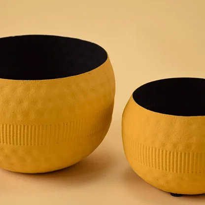 Closeup of yellow round textured pot shown with other pots highlighting detailed surface texture and matte black interior.