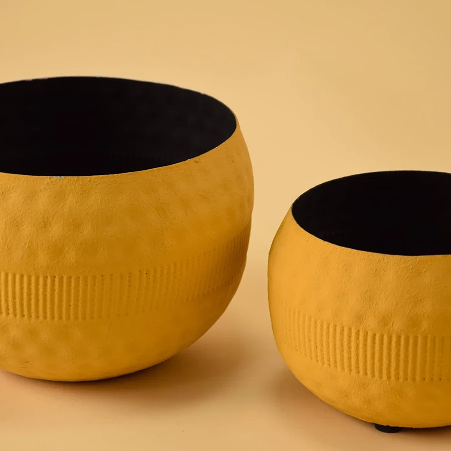 Closeup of yellow round textured pot shown with other pots highlighting detailed surface texture and matte black interior.