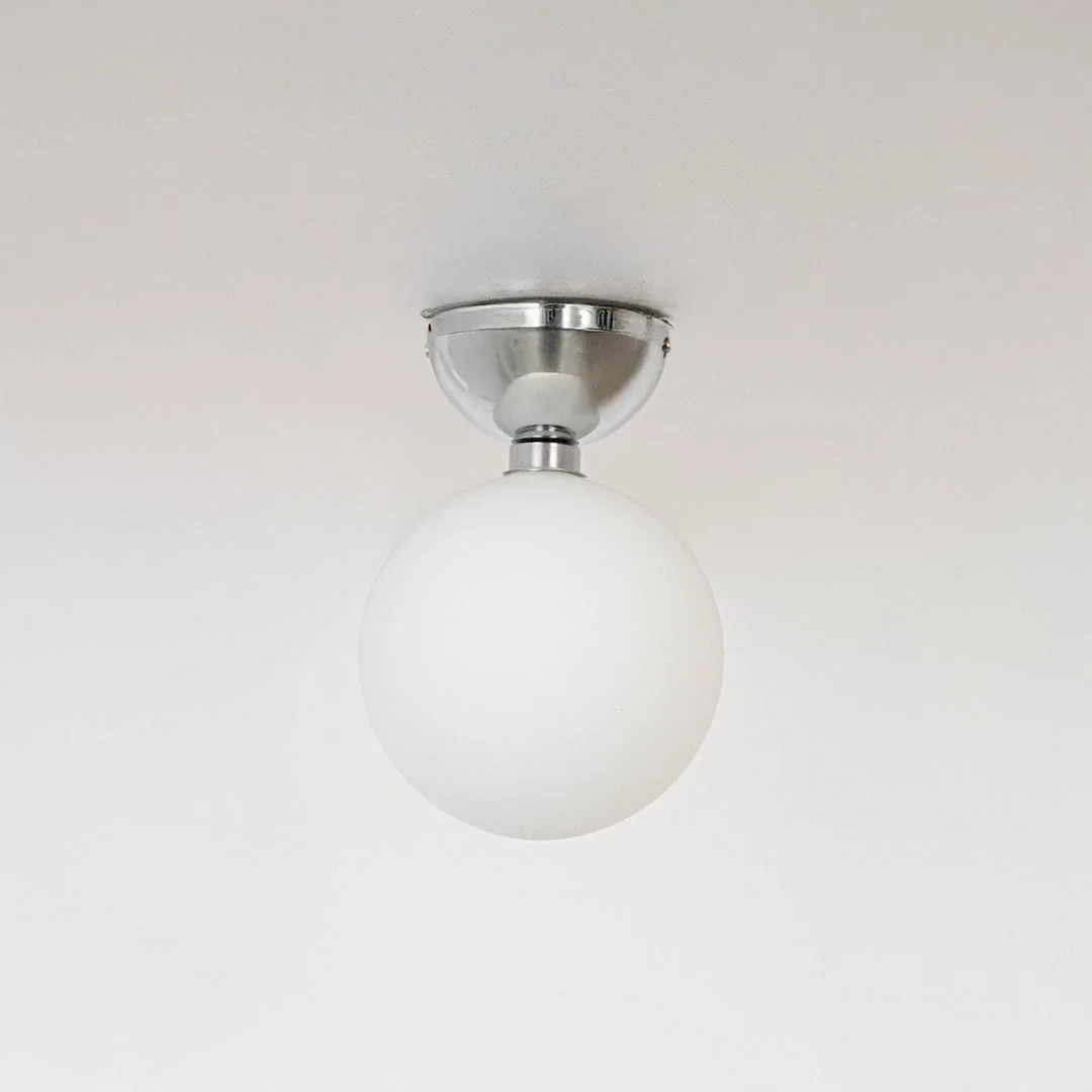 Ceiling light with polished chrome base and frosted glass globe shade shown off on plain white background.