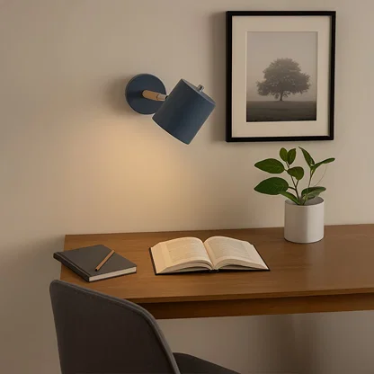 A soft warm glow from a blue wall lamp illuminates a cozy study corner with a wooden desk an open book a plant in a white pot and a framed artwork on a light wall.