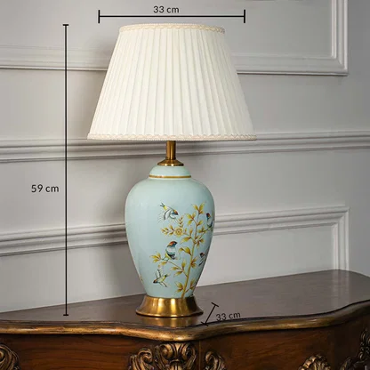 Ceramic table lamp 59 cm height 33 cm width with pleated shade blue base floral bird pattern and gold finish light off white background.
