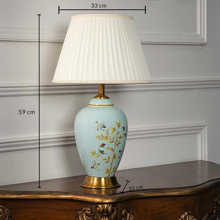 Ceramic table lamp 59 cm height 33 cm width with pleated shade blue base floral bird pattern and gold finish light off white background.