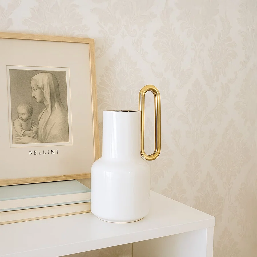 White ceramic vase with a gold handle styled in a modern interior perfect for consoles shelves and elegant contemporary home decor accents.