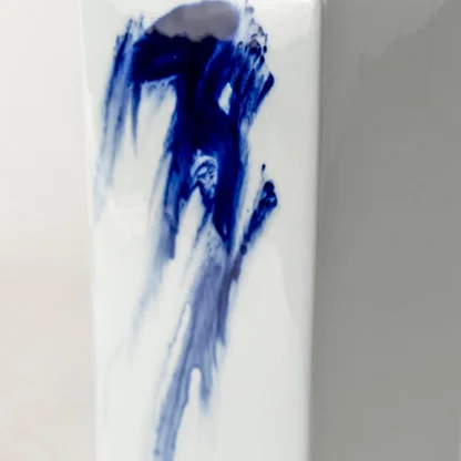Tall white ceramic jar with vivid blue abstract brush design captured on smooth background for décor accents.