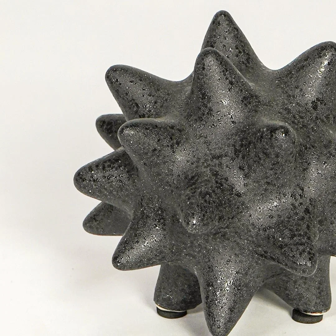 Close view of black ceramic decorative object highlighting rough textured finish and bold geometric spiked design.