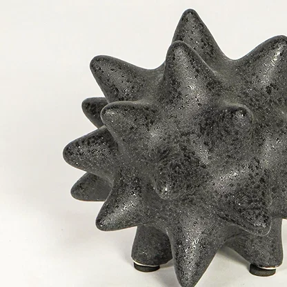 Close view of black ceramic decorative object highlighting rough textured finish and bold geometric spiked design.