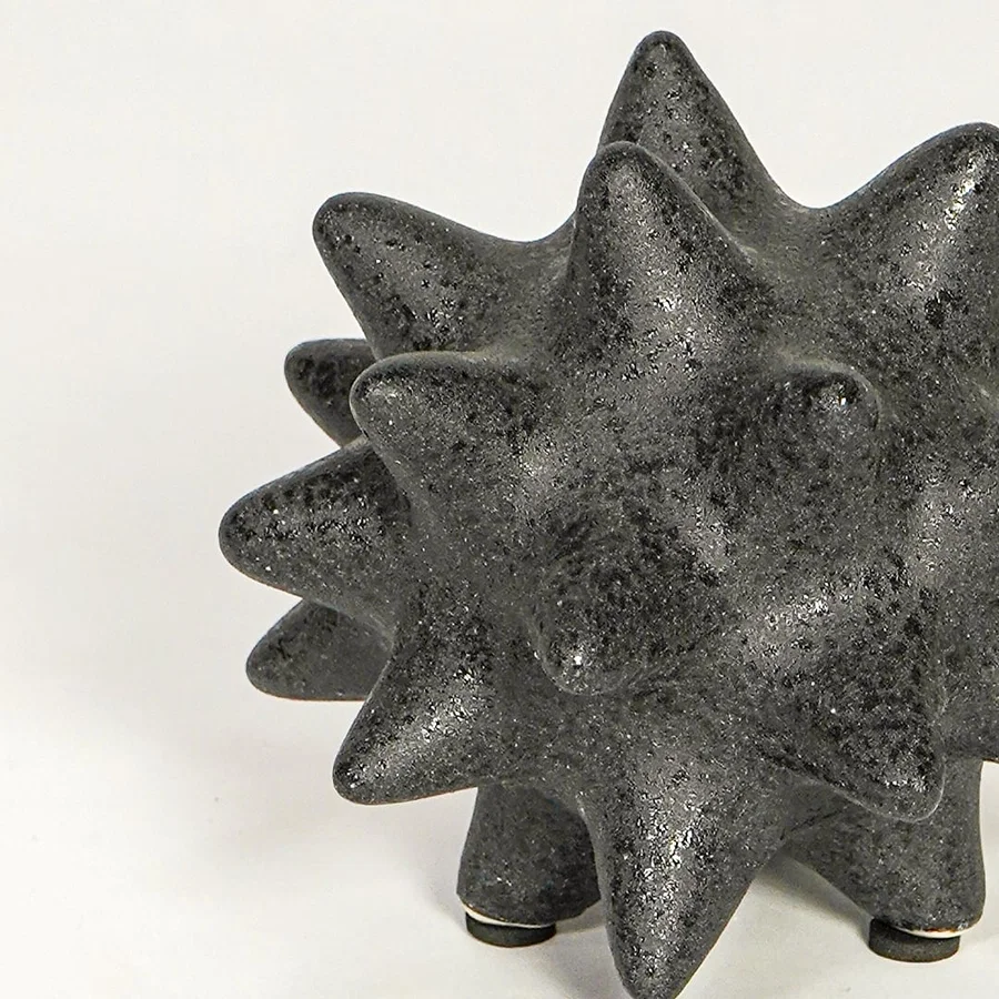 Close view of black ceramic decorative object highlighting rough textured finish and bold geometric spiked design.