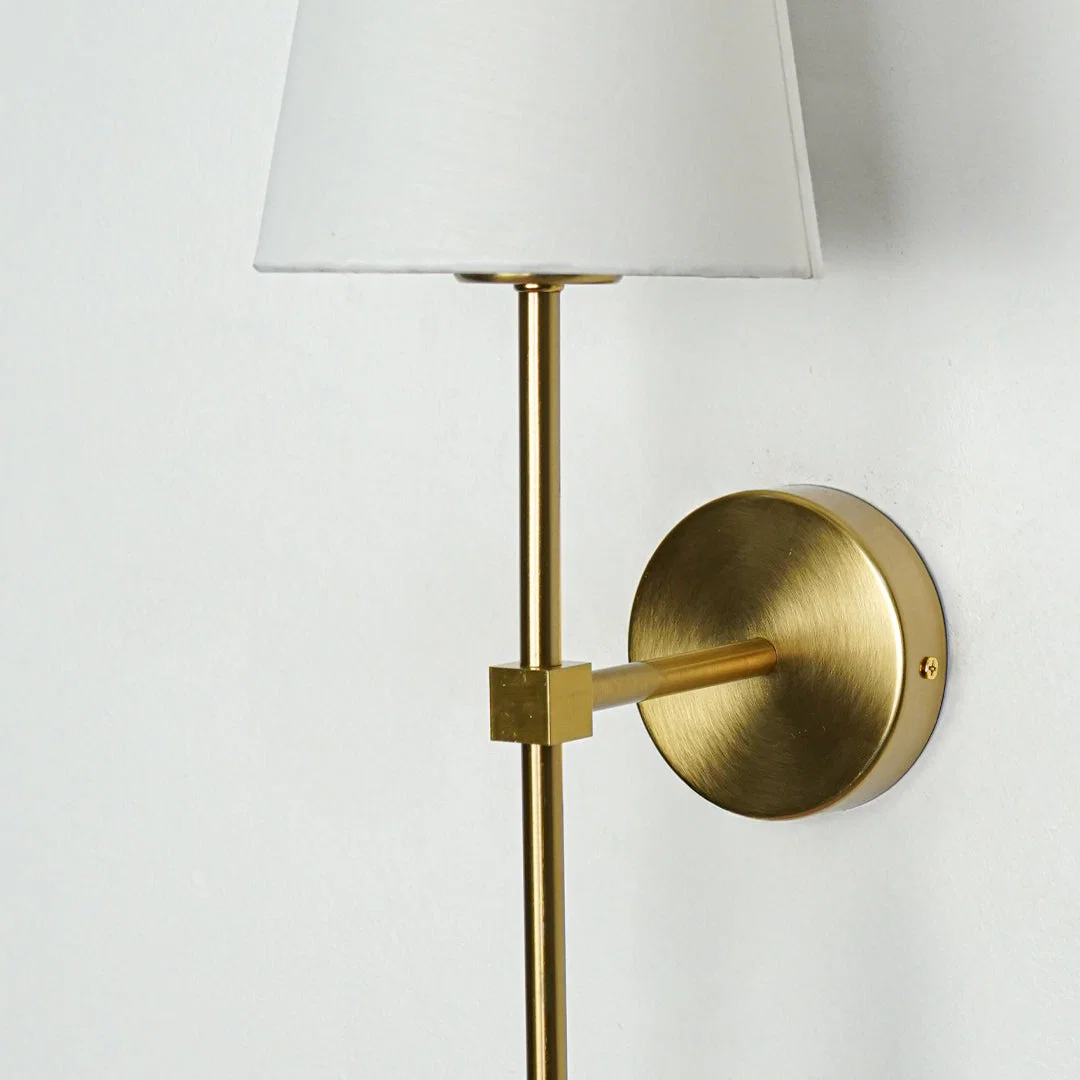 Contemporary wall light in gold metal finish with fabric shade for bedroom or living decor lighting white background.