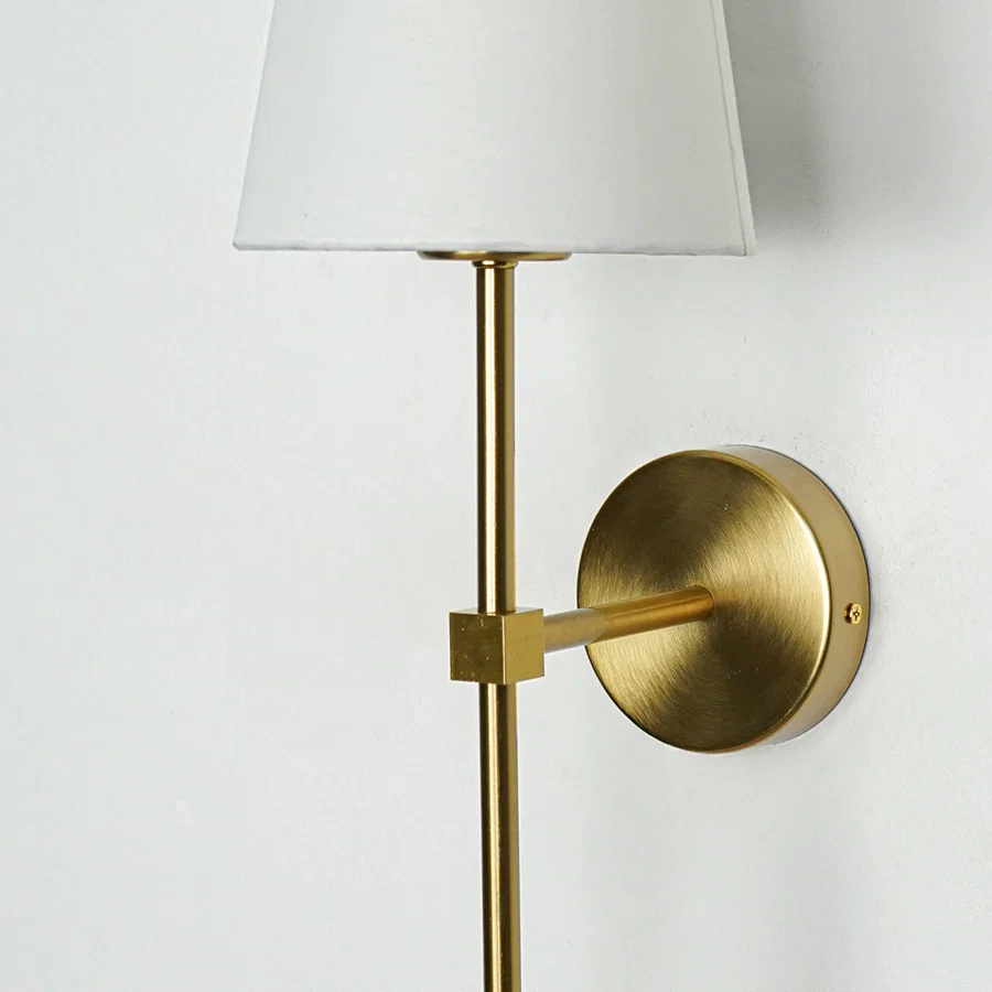 Contemporary wall light in gold metal finish with fabric shade for bedroom or living decor lighting white background.