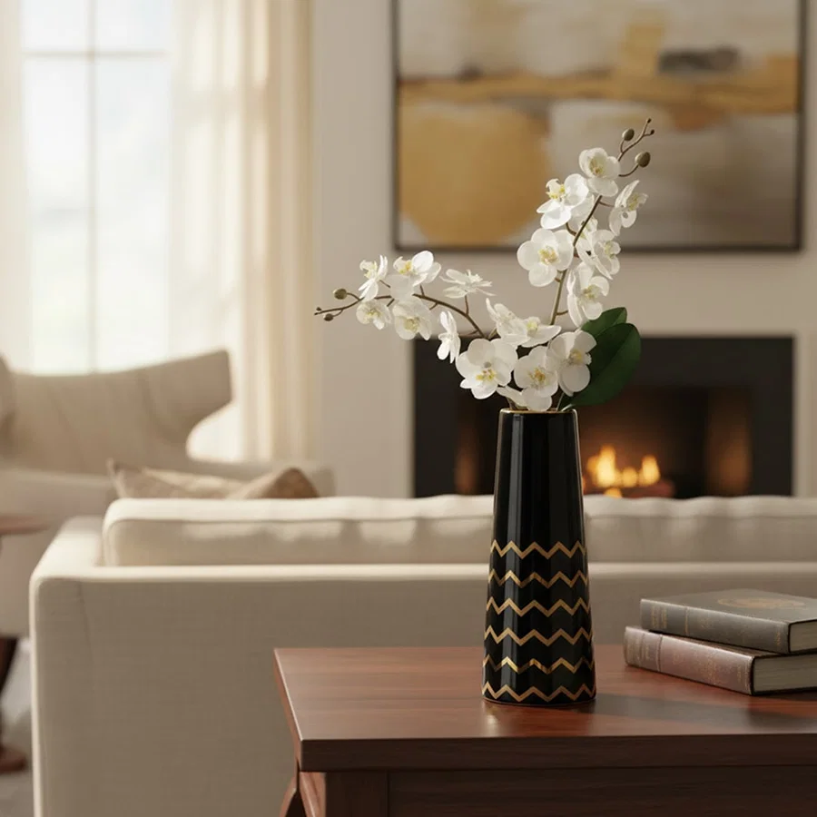 A tall black ceramic vase with gold zigzag detailing styled on a clean white surface creating a bold modern decor highlight in the scene.