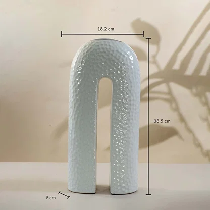 White ceramic arch-shaped vase with hammered finish shown with 38.5 cm height and 18.2 cm width measurement detail.