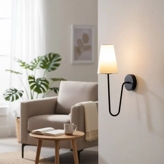 Minimalist black curved gooseneck wall lamp with a white cone shade illuminating a cozy living room armchair space.