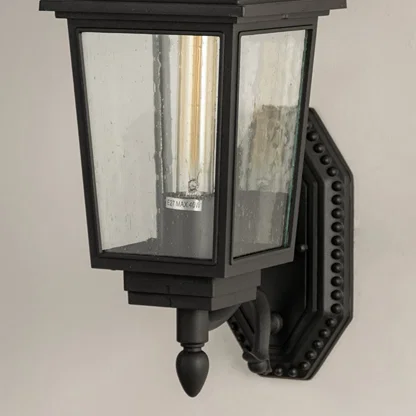 Closeup of black metal outdoor lantern showing clear textured glass panels and detailed vintage style frame for refined exterior lighting.