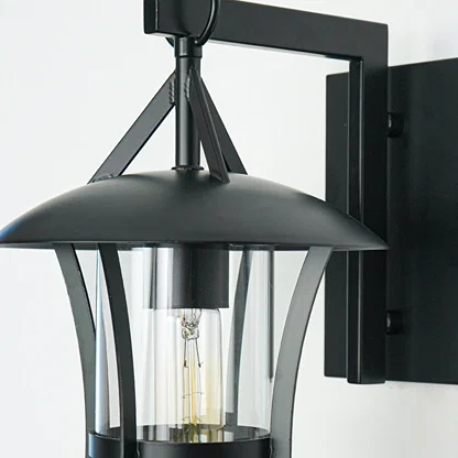 Close view of black metal wall lantern with curved arm and clear glass shade showcasing durable outdoor lighting design on neutral background.