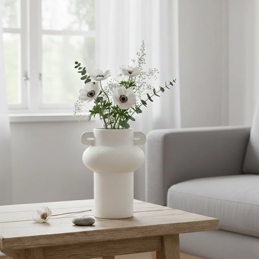 White textured ceramic decorative vase with flowers placed on wooden coffee table in modern living room interior styling.