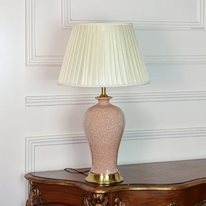 Elegant pink ceramic table lamp with textured body gold metal base and pleated fabric shade on soft off white background.