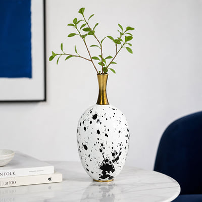 White and black ceramic flower vase with gold neck placed on marble table for elegant home decor.