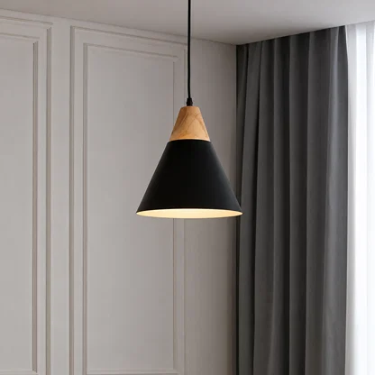 A modern pendant light with a matte black cone shade and a natural light wood top, hanging in a room with gray curtains and white paneled walls.