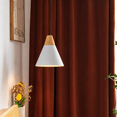 A modern pendant light with a white cone shade and natural wood accents hangs in front of dark rust-brown curtains in a styled interior setting.