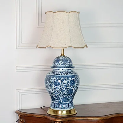 Classic blue white ceramic table lamp with ornate floral design brass base and fabric shade on off white background.