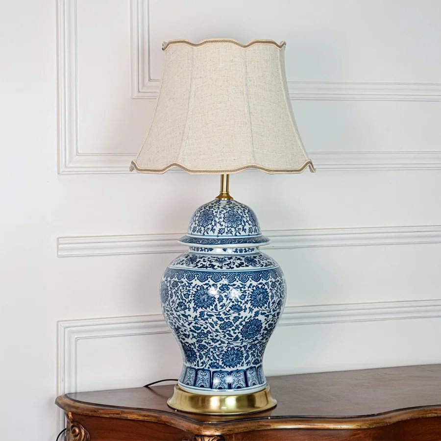 Classic blue white ceramic table lamp with ornate floral design brass base and fabric shade on off white background.