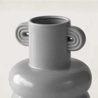 Closeup of white ceramic vase with sculptural handles showcasing premium craftsmanship and modern decorative styling.