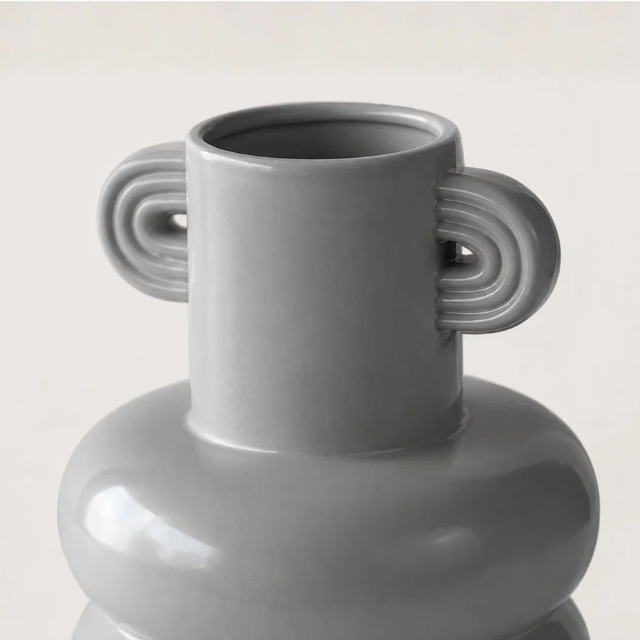 Closeup of white ceramic vase with sculptural handles showcasing premium craftsmanship and modern decorative styling.