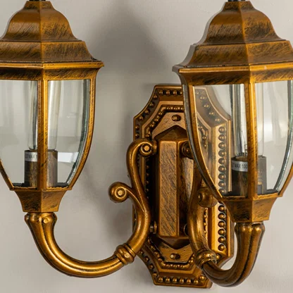 Closeup view of double brass outdoor lantern showing glowing bulbs clear glass panels and antique metal finish for warm elegant entrance lighting.